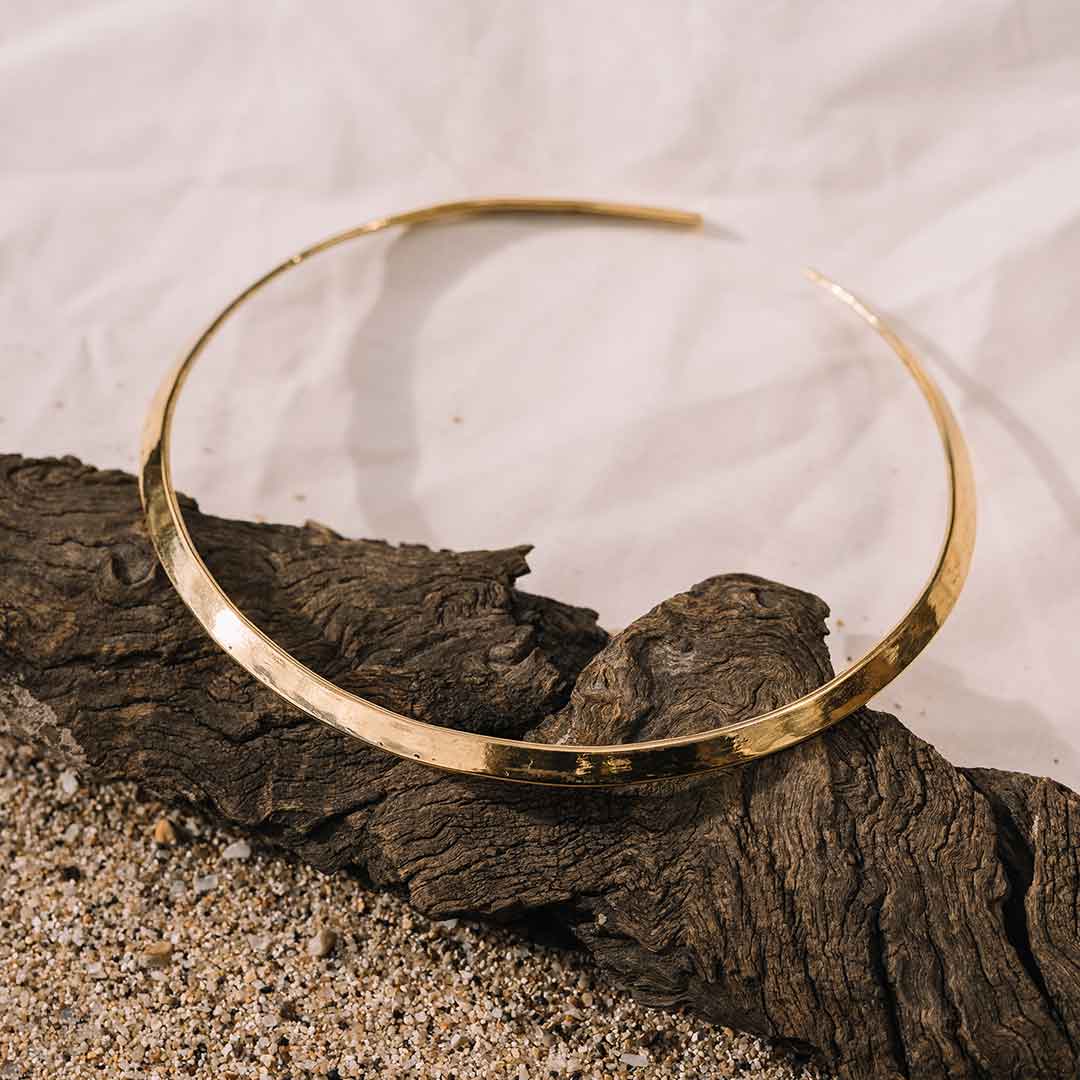 Auf diesem Bild liegt der goldene Messing Halsreif auf eine Stück Holz.