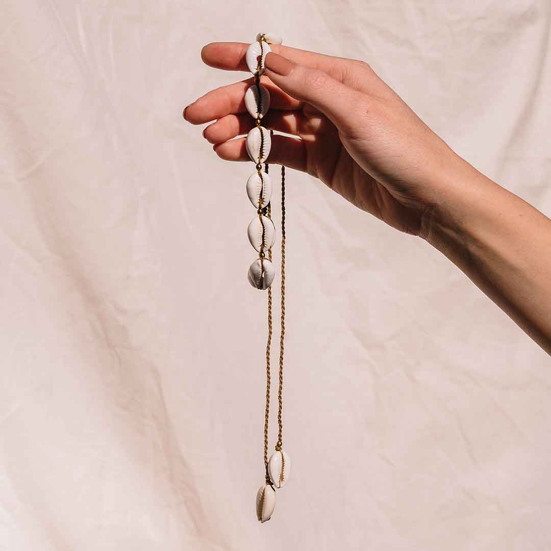 Auf diesem Bild wird die Kauri Muschelkette von einer Hand gehalten.